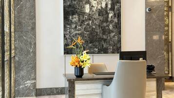 Un interior moderno con una pared de mármol, un cuadro abstracto grande, un escritorio con una silla y un jarrón de flores.