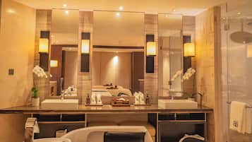 A modern bathroom with a large mirror, two sinks, a bathtub, and a shower.