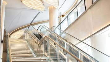 A modern interior with a curved staircase, glass railings, and a high ceiling with lighting fixtures.