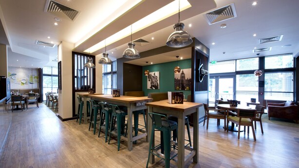 Een modern restaurantinterieur met houten vloeren, groene barkrukken en hanglampen.