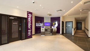 Een hotel lobby met een receptiebalie, incheckautomaten en een bord met de tekst 'Premier Inn Good Night Guarantee'.