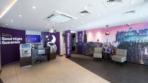 A hotel lobby with a reception desk, a check-in counter, and a seating area with a cityscape mural. - Premier Inn Edinburgh Cc York Place/St James Quarter (Edinburgh)