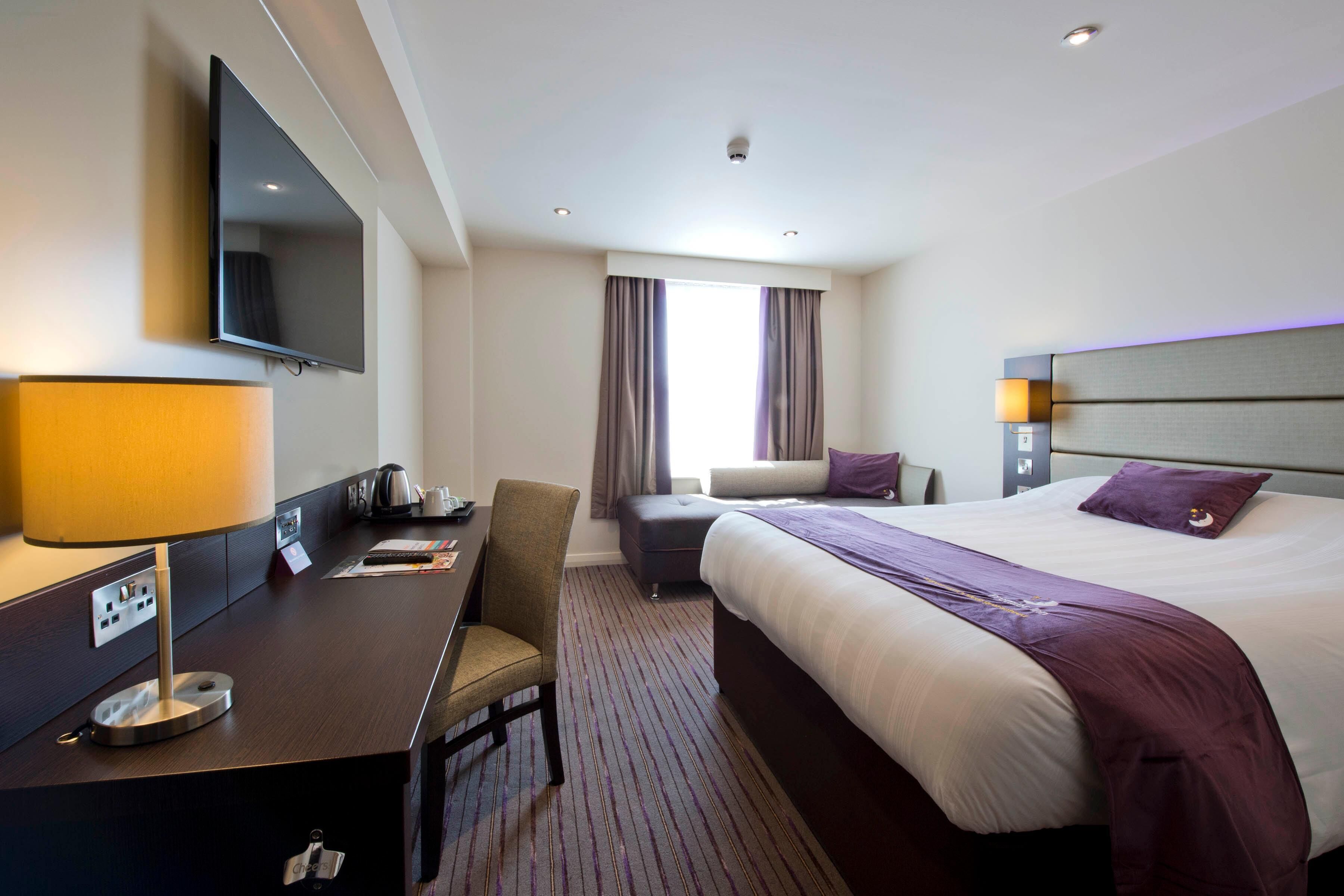 A hotel room with a bed, desk, chair, TV, and a window with curtains.