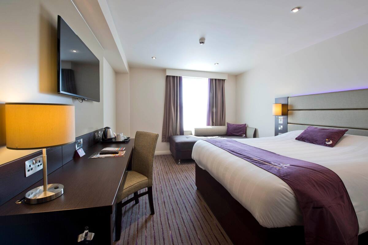 A hotel room with a bed, desk, chair, TV, and a window with curtains.