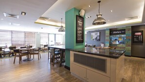 A modern restaurant with a bar area, wooden tables, and a kitchen counter. - Premier Inn Penrith (Penrith)