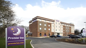 Ett Premier Inn-hotell med en skylt, en parkeringsplats och en byggnad med flera fönster.