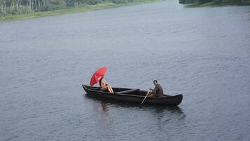 A calm lake with a boat carrying two people, one holding a red umbrella.