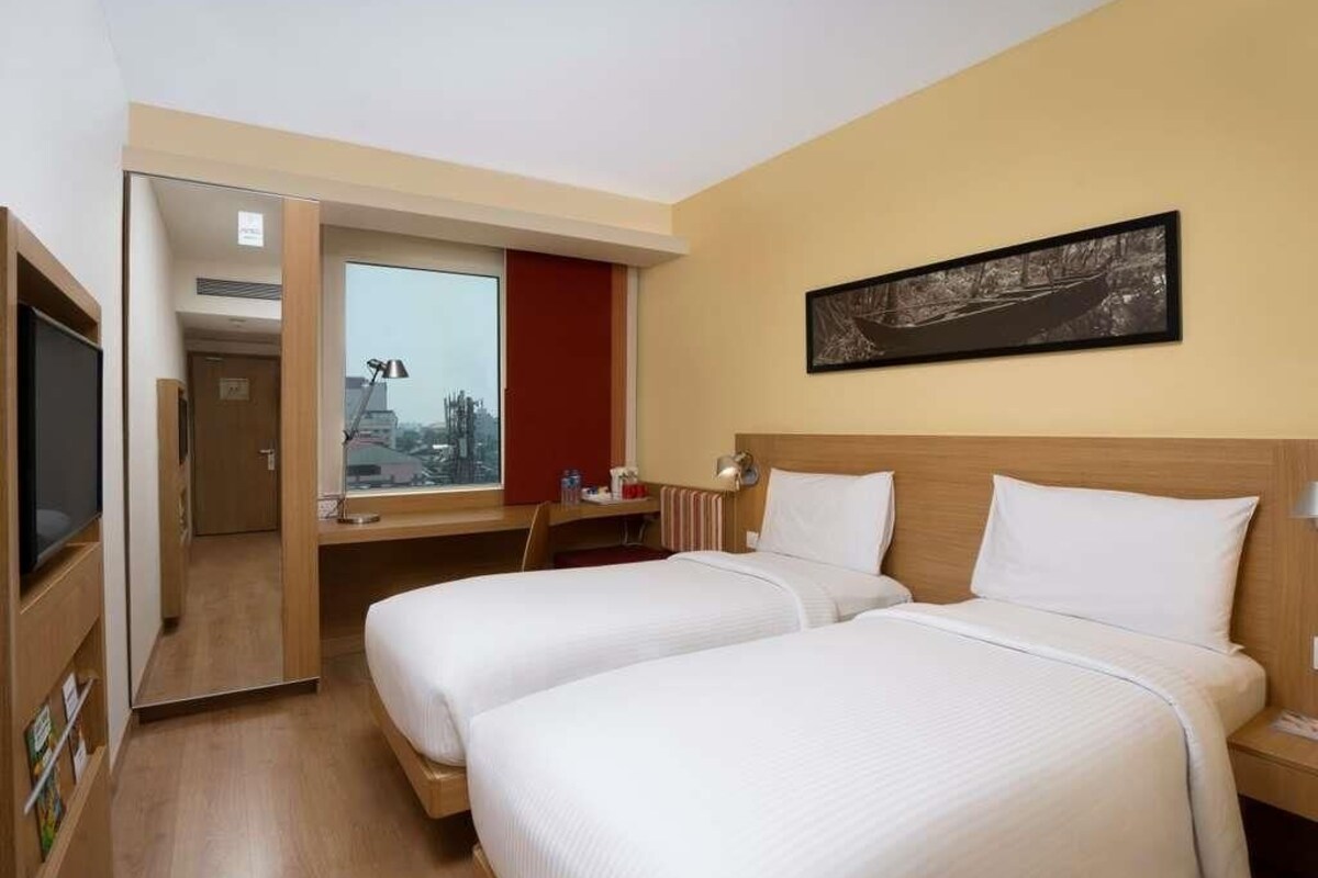 Ett hotellrum med två sängar, ett skrivbord, en TV och ett fönster med utsikt över staden.
