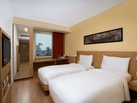 Habitación de hotel con dos camas, un escritorio, televisión y ventana con vistas a la ciudad.