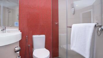Un baño con inodoro blanco, lavamanos, cabina de ducha de vidrio y una toalla colgada en la puerta de la ducha.