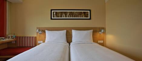 Una cama doble con cabecera de madera, dos mesitas de noche con lámparas, un banco rojo y un cuadro en la pared.