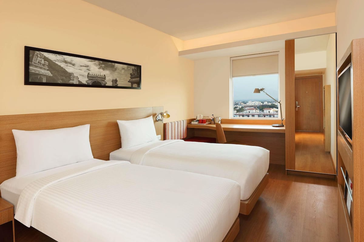 A hotel room with two beds, a desk with a lamp, a television, and a framed picture on the wall.