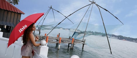 A person standing by a waterfront with fishing nets and a red umbrella.