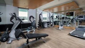 Ein modernes Fitnessstudio mit unterschiedlichen Trainingsgeräten, großen Fenstern und einer Holzbalkendecke.