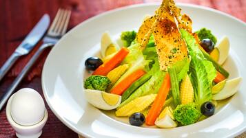 A plate of mixed vegetables including broccoli, carrots, and corn, with a small bowl of dressing on the side.