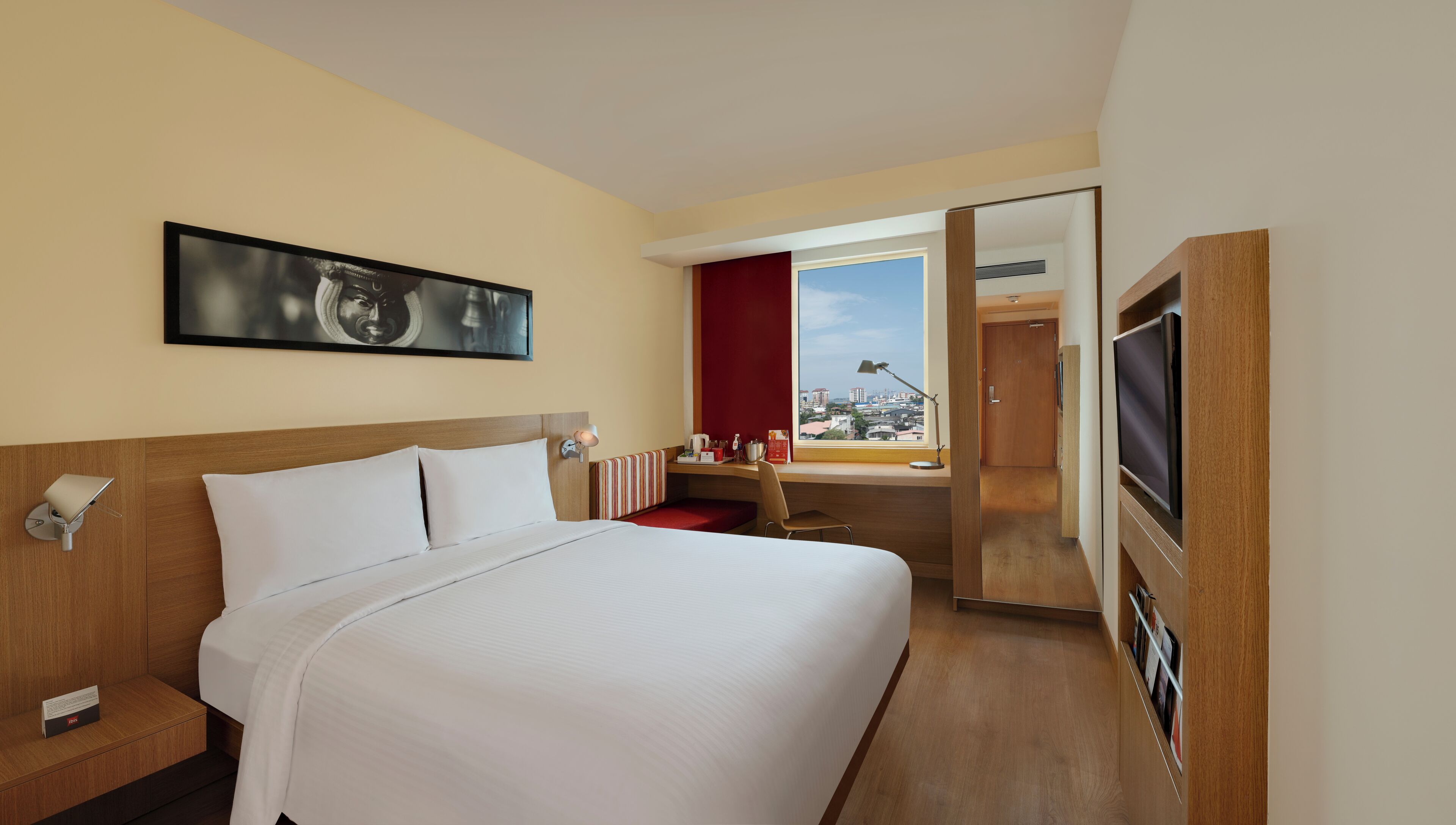 Habitación de hotel con cama, escritorio, televisor y ventana con vista a la ciudad.