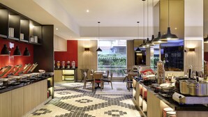 A modern kitchen with a buffet setup, a dining area with chairs, and a view through the window. - ibis Melaka (Malacca City)