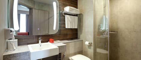 Een moderne badkamer met een grote spiegel, een witte wastafel, een toilet en een douchecabine met glazen wanden.