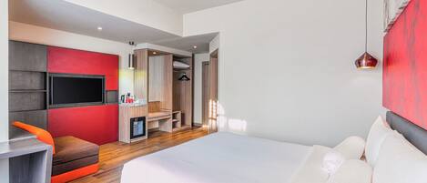 A modern hotel room with a large bed, a seating area with a TV, and a walk-in closet.