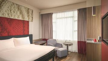 Habitación de hotel con una cama grande, una mesita, una silla y un escritorio con tetera.