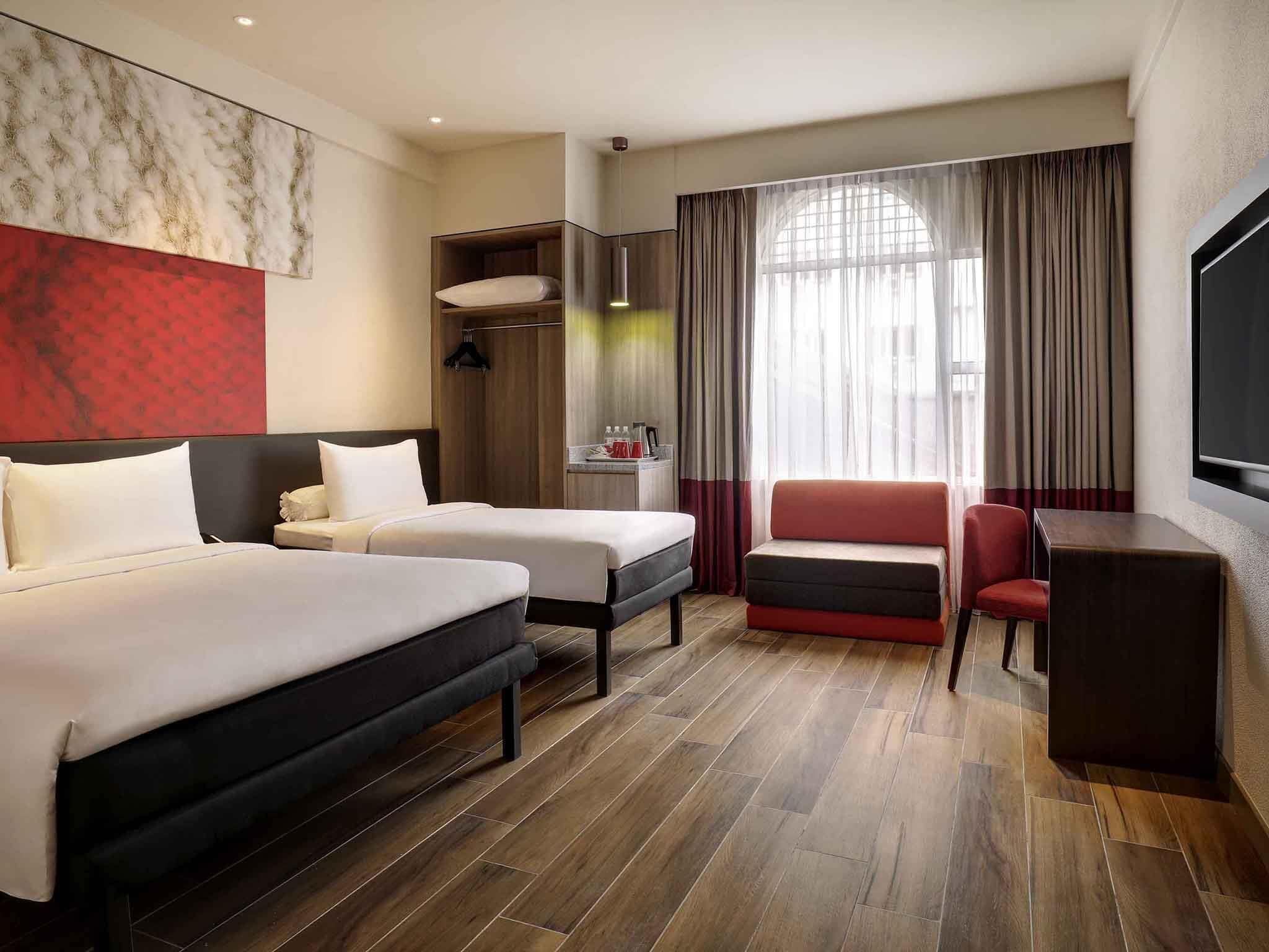 Une chambre d’hôtel avec deux lits, un bureau, une chaise, une télévision et une fenêtre avec des rideaux.