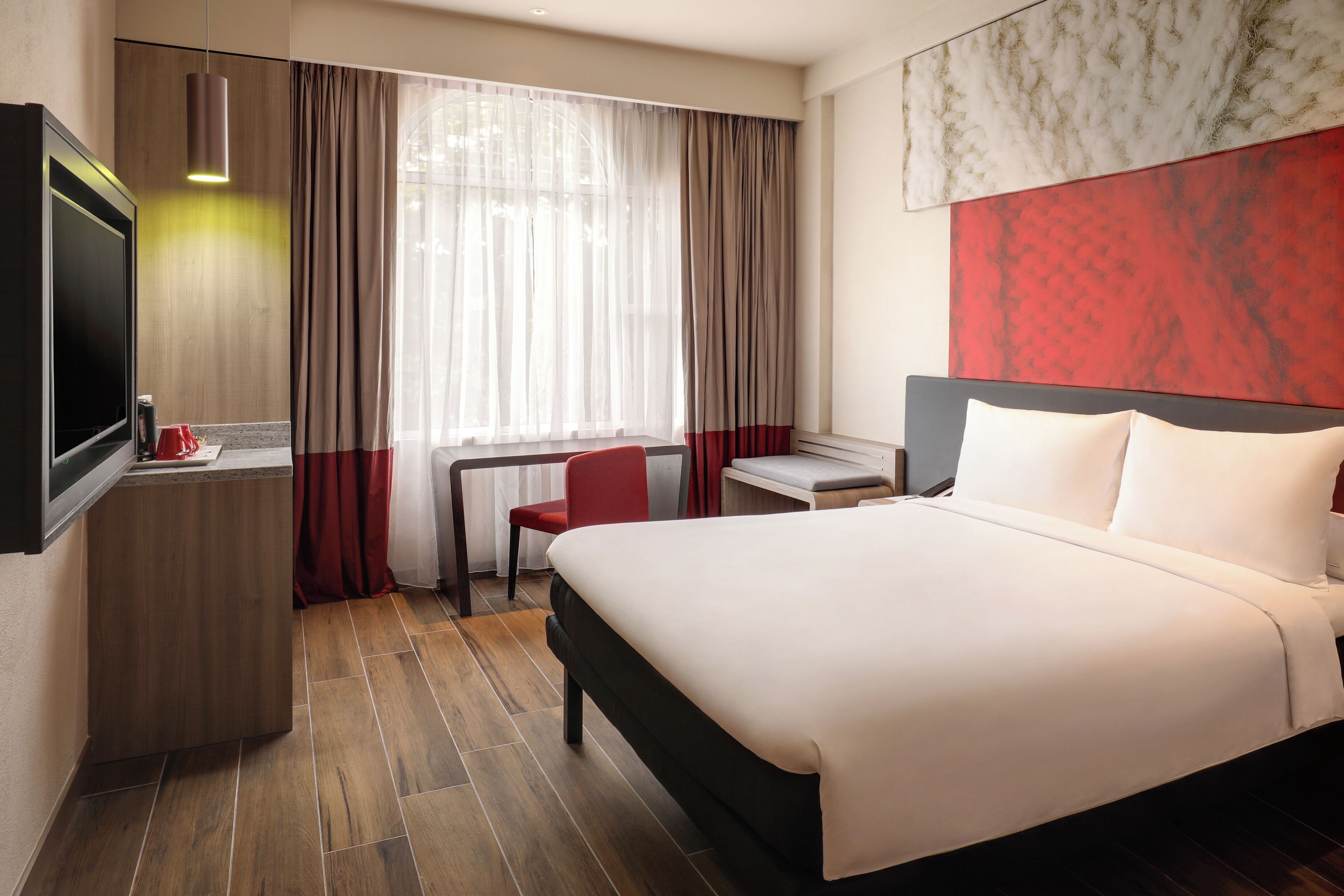 A hotel room with a bed, a desk, a chair, and a TV.