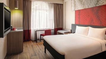 A hotel room with a bed, a desk, a chair, and a TV.