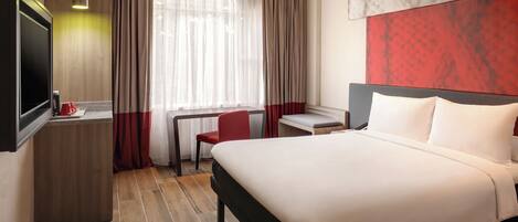 A hotel room with a bed, a desk, a chair, and a TV.