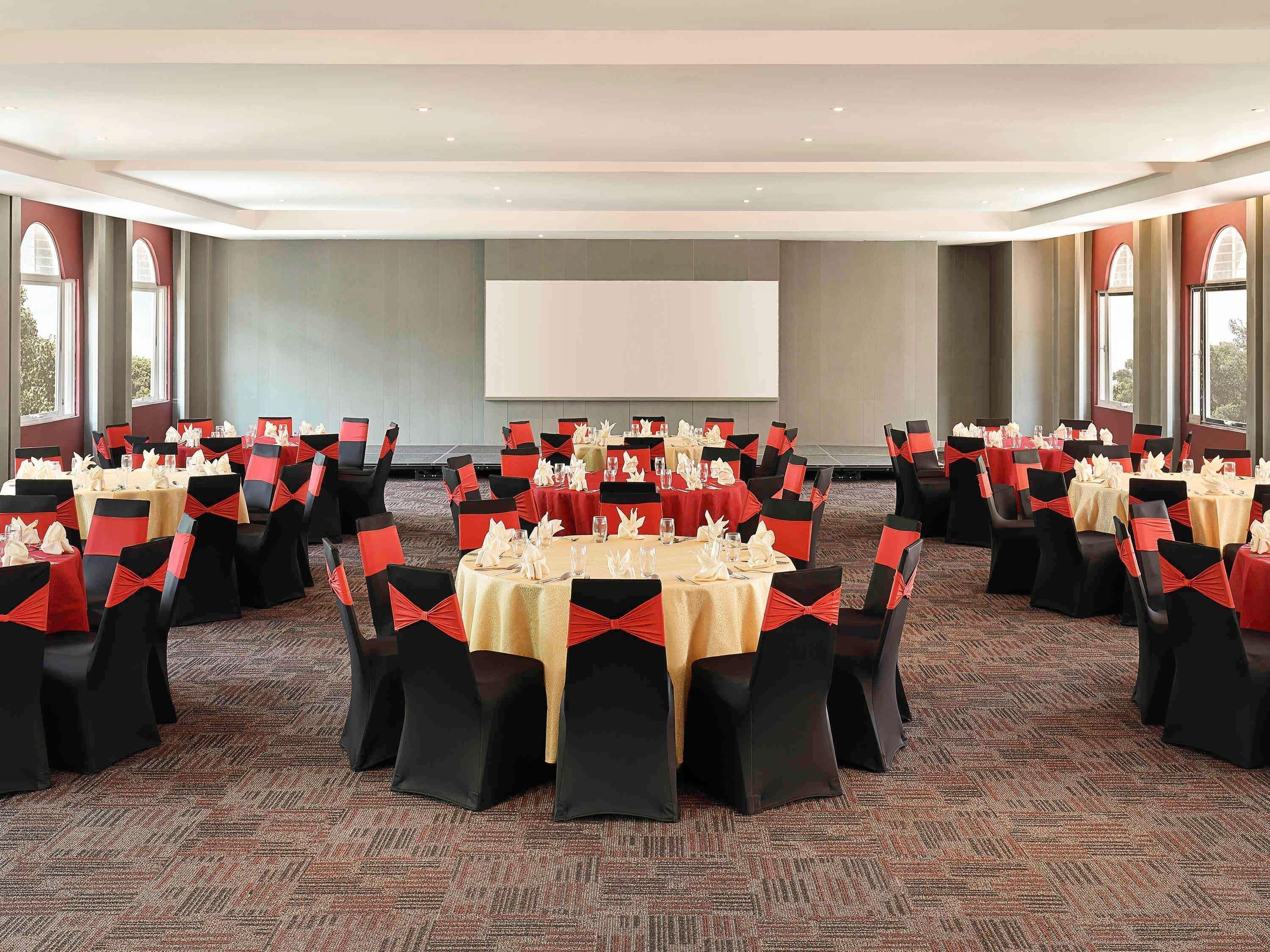 A conference room with multiple tables and chairs, arranged in rows, with a large screen at the front.
