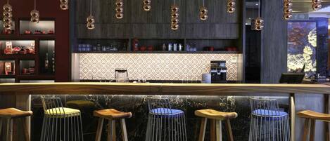 Zona de bar con taburetes de madera, encimera de mármol e iluminación colgante esférica.