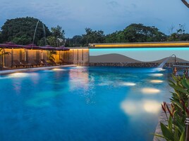 A swimming pool with lounge chairs and umbrellas, surrounded by a stone wall and greenery.