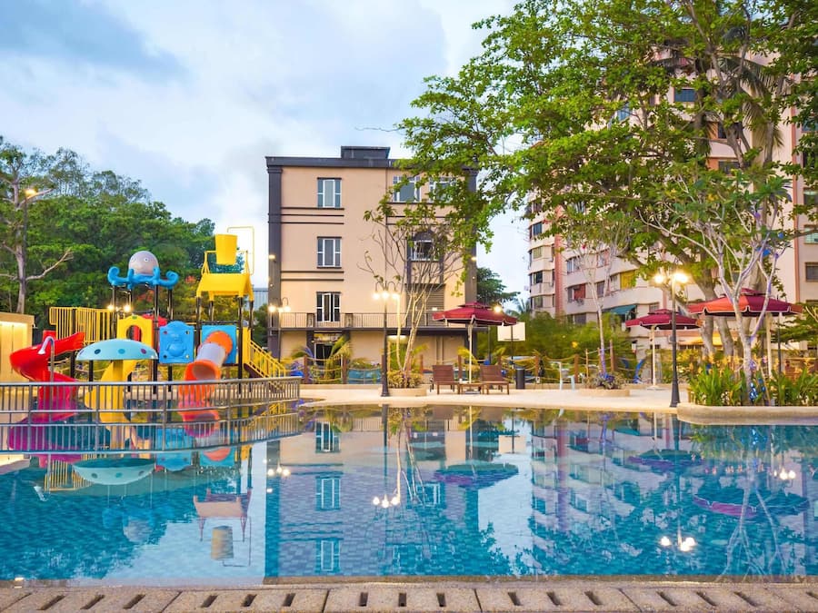 Ein Schwimmbad mit einem Spielbereich für Kinder, umgeben von Gebäuden und Bäumen.