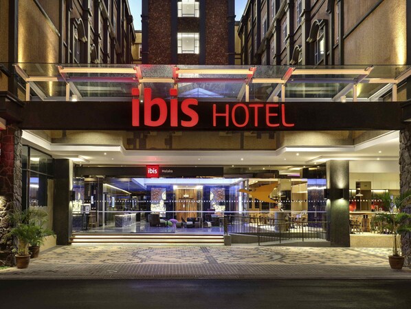 The exterior of the ibis hotel with a modern facade, large glass entrance, and a well-lit lobby area. - ibis Melaka (Malacca City)