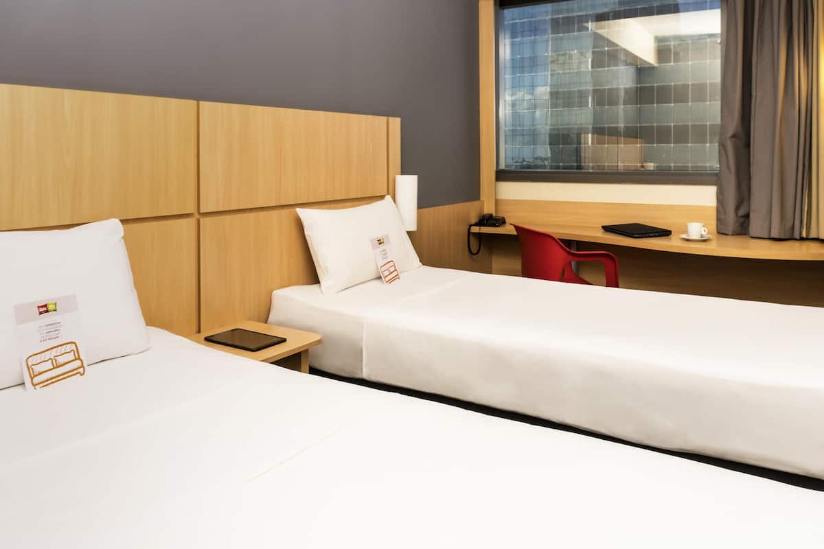 A hotel room with two beds, a desk, a chair, a phone, and a window with curtains.