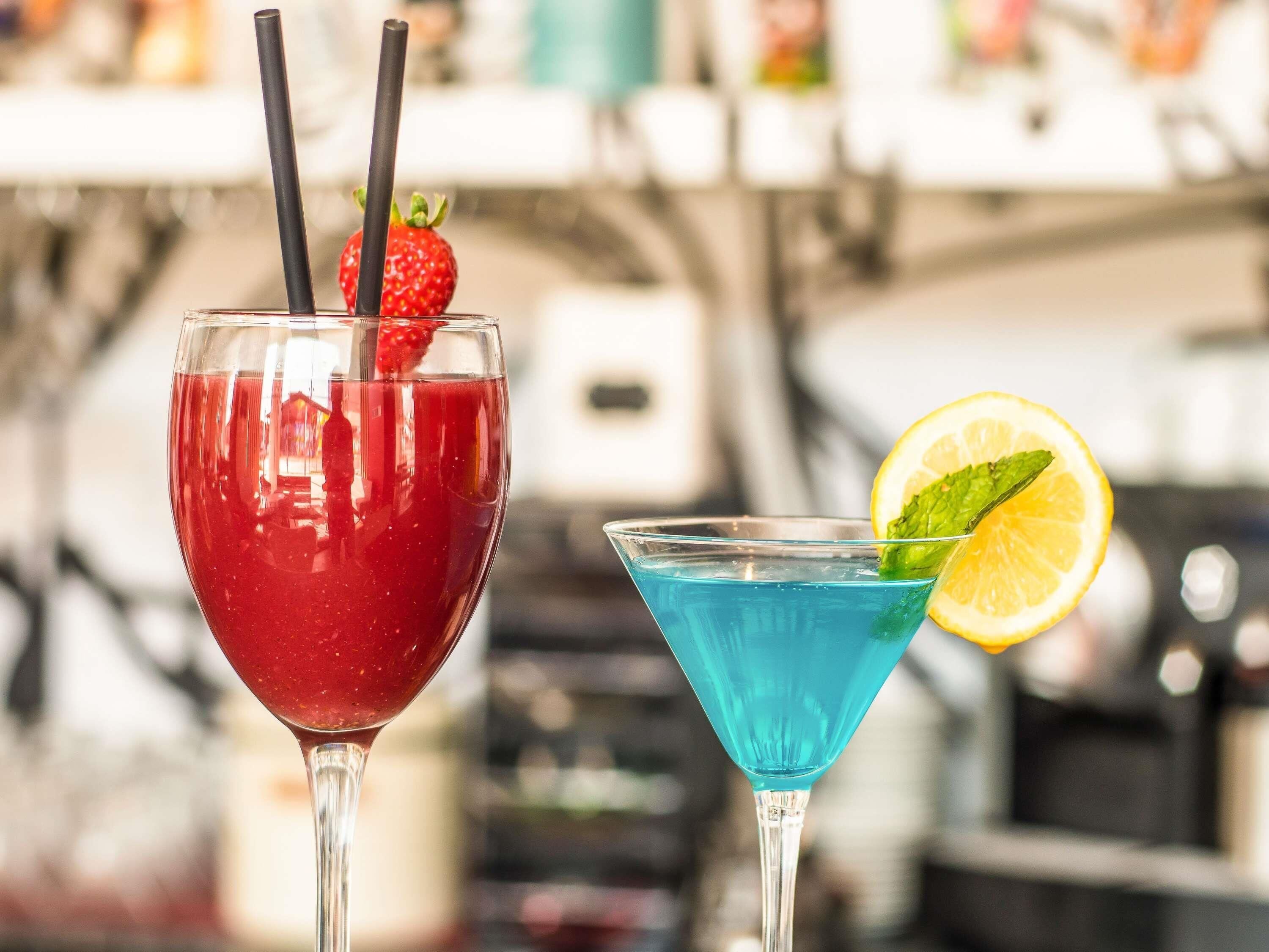 Deux cocktails servis dans des verres, avec des pailles et des décorations, sur un fond flou.