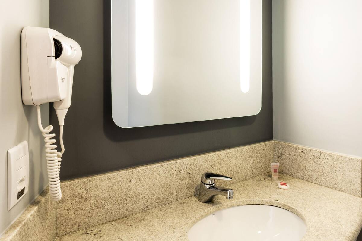 A bathroom with a white sink, a mirror, a hairdryer, and a faucet.