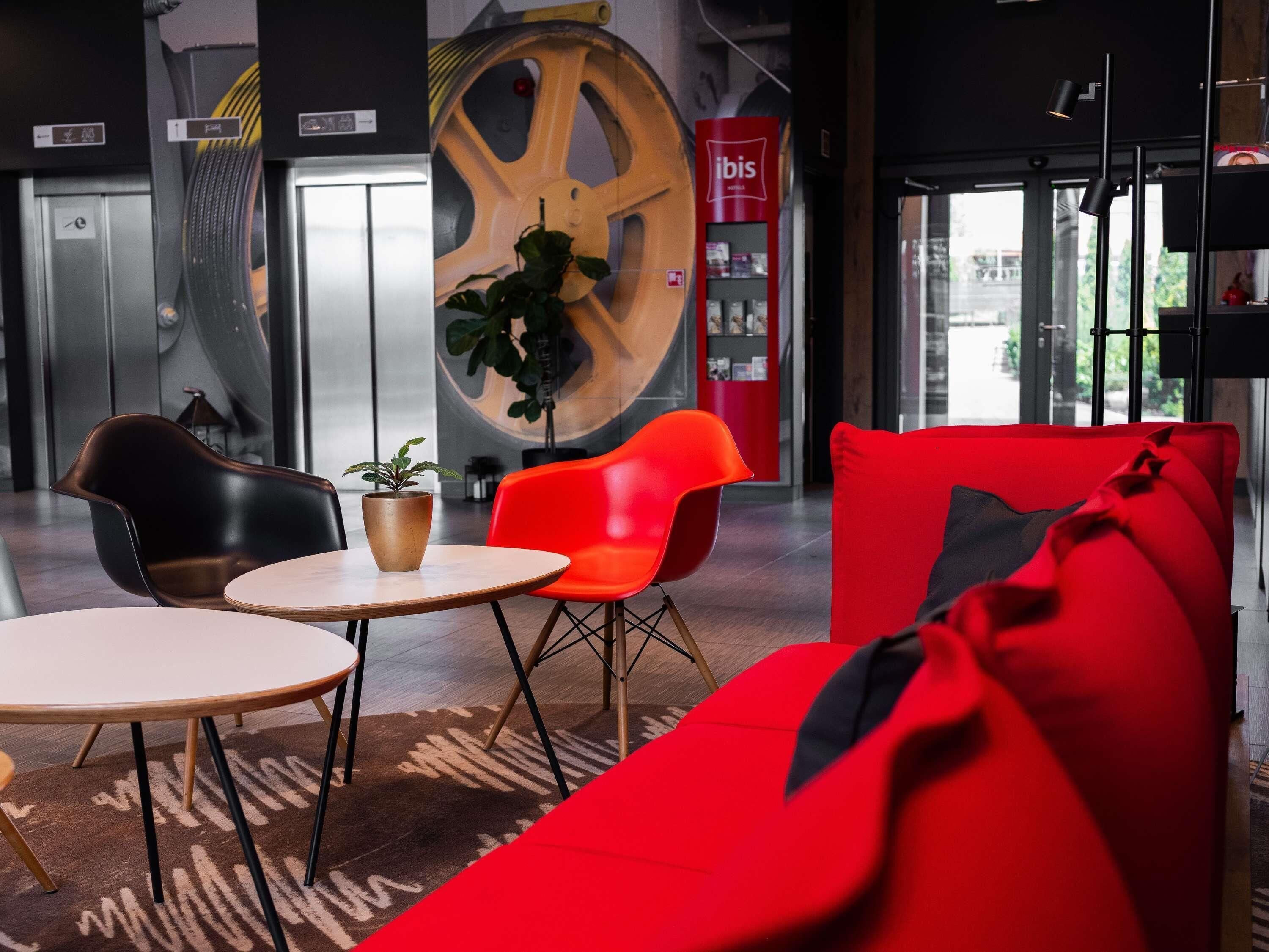 A modern lobby with a red sofa, black and red chairs, a wooden table, and a large wheel decoration.