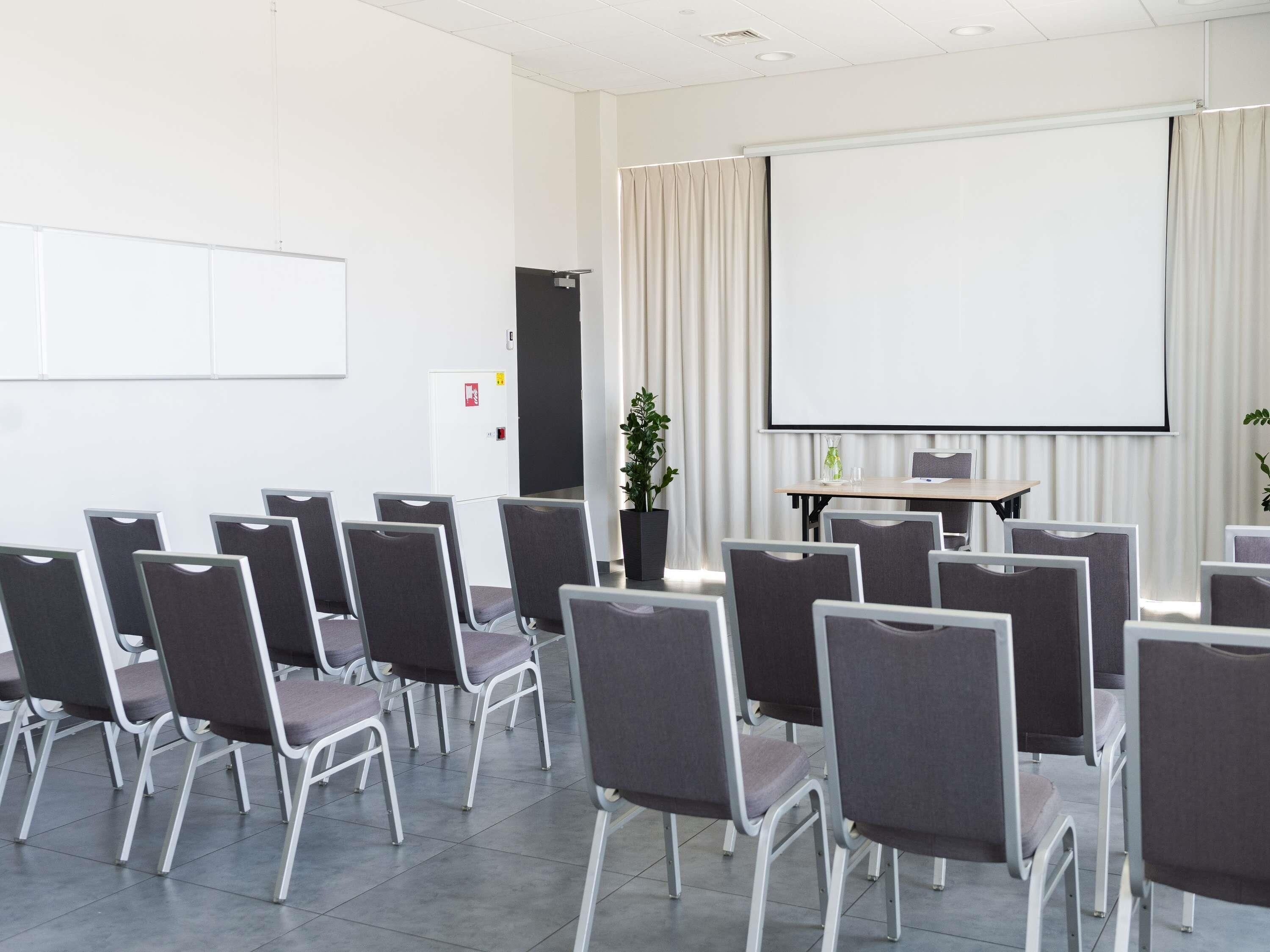 Un salón de conferencias con filas de sillas, una pantalla de proyector y una pizarra.