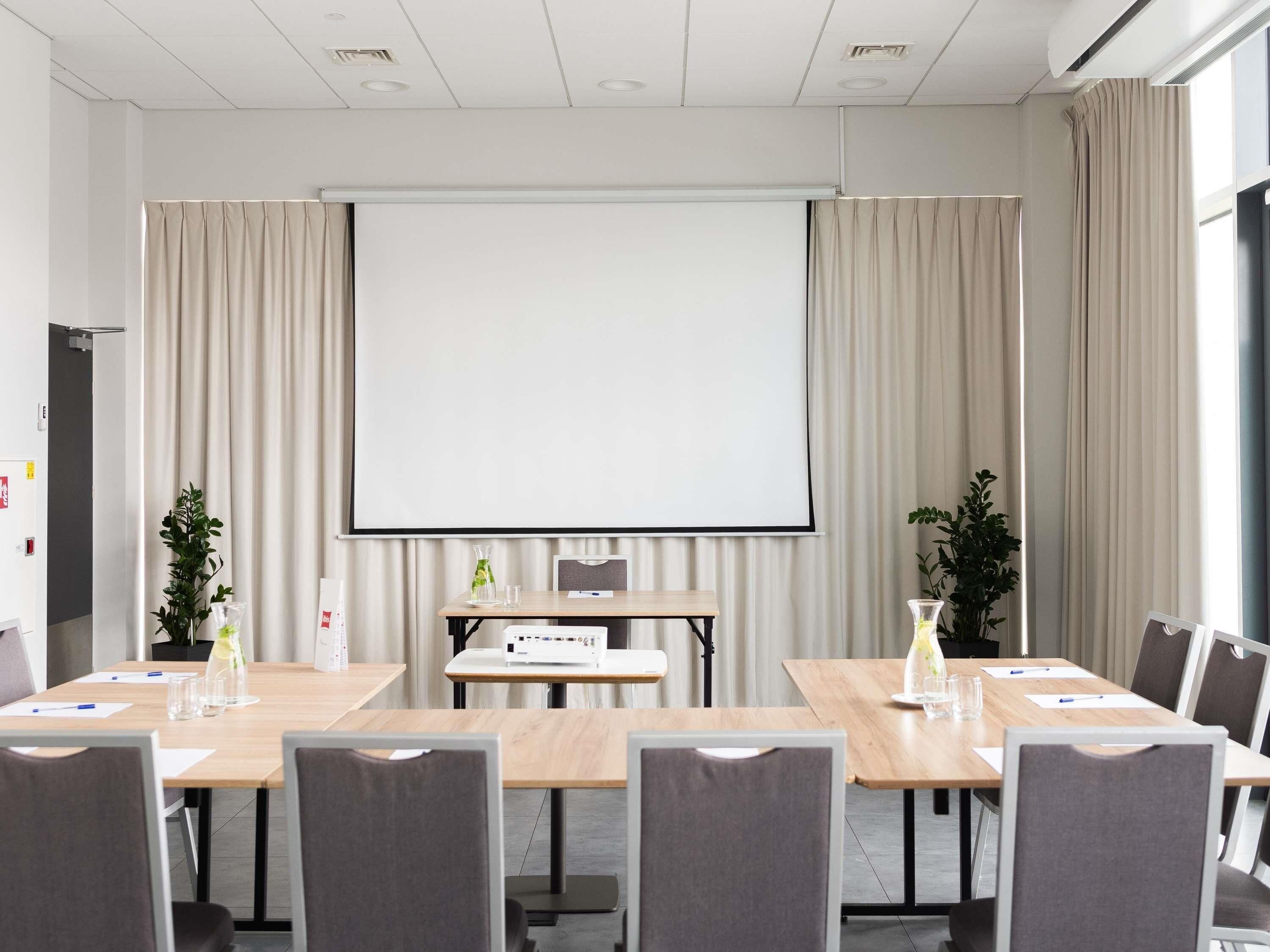 A conference room with a large projection screen, wooden tables, and chairs.