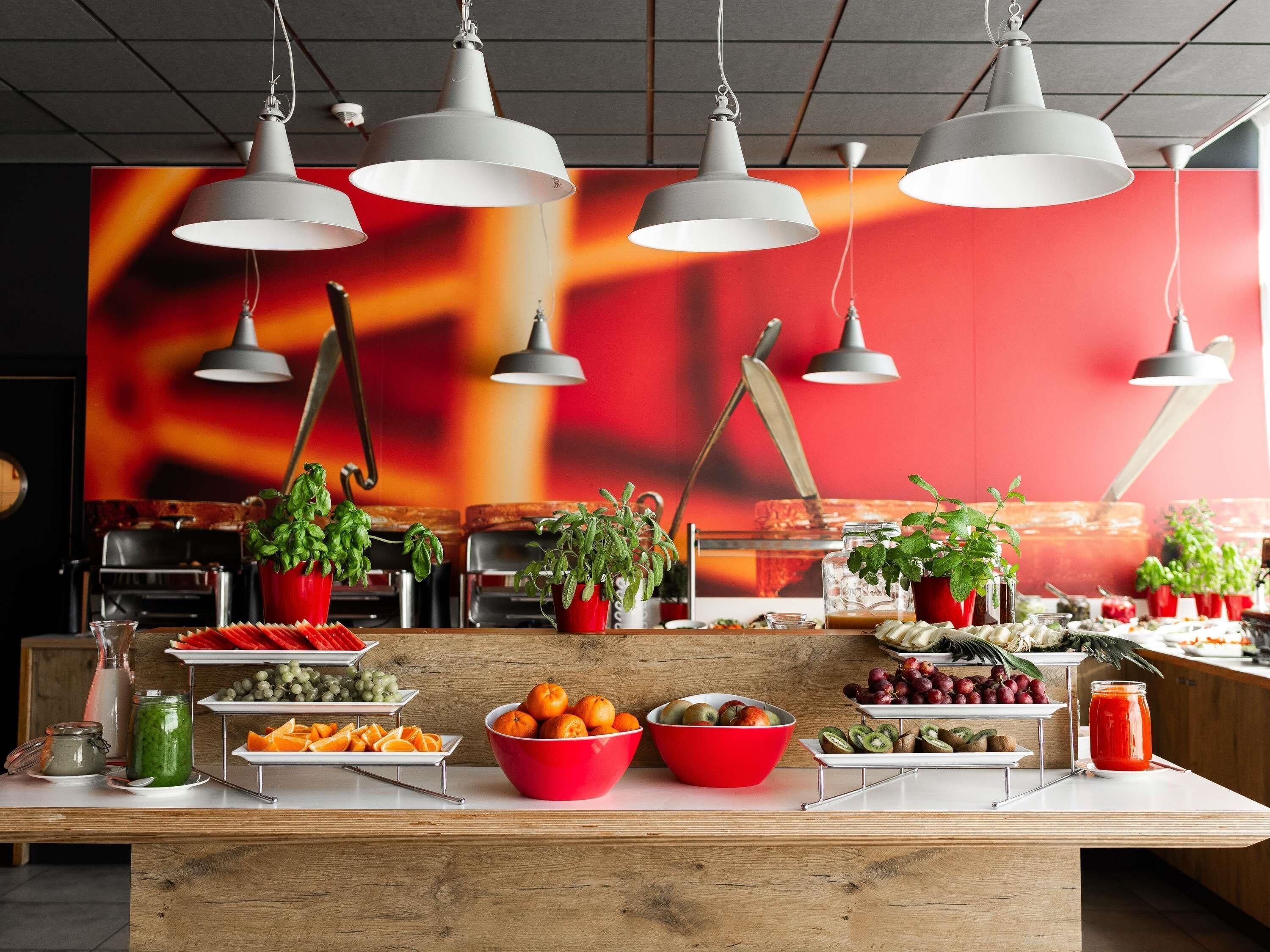 A buffet setup with various fruits and vegetables, multiple hanging pendant lights, and potted plants.