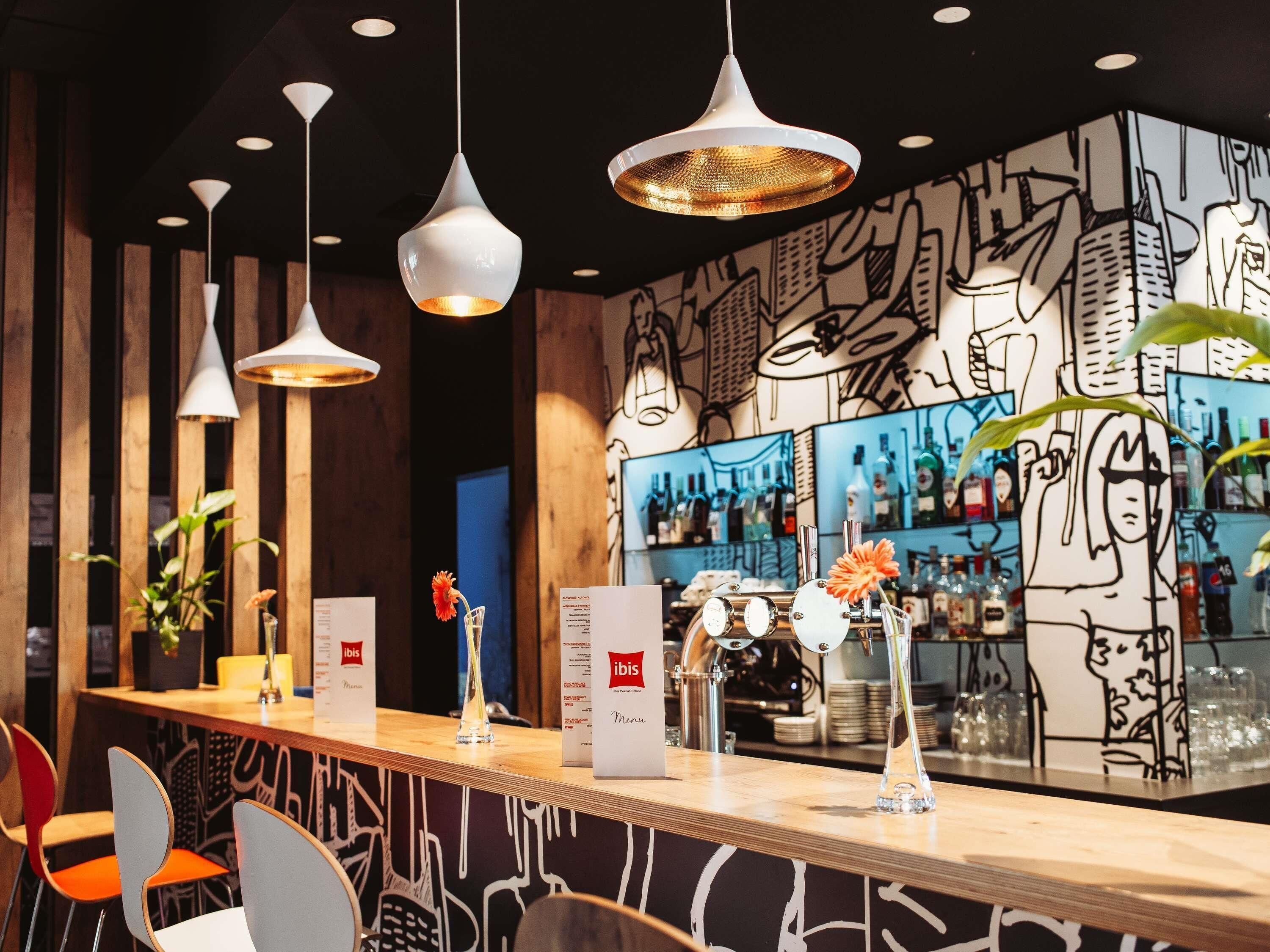 Eine Bar mit hängenden Pendelleuchten, einer Holztresen und einer Wand mit Wandgemälde.