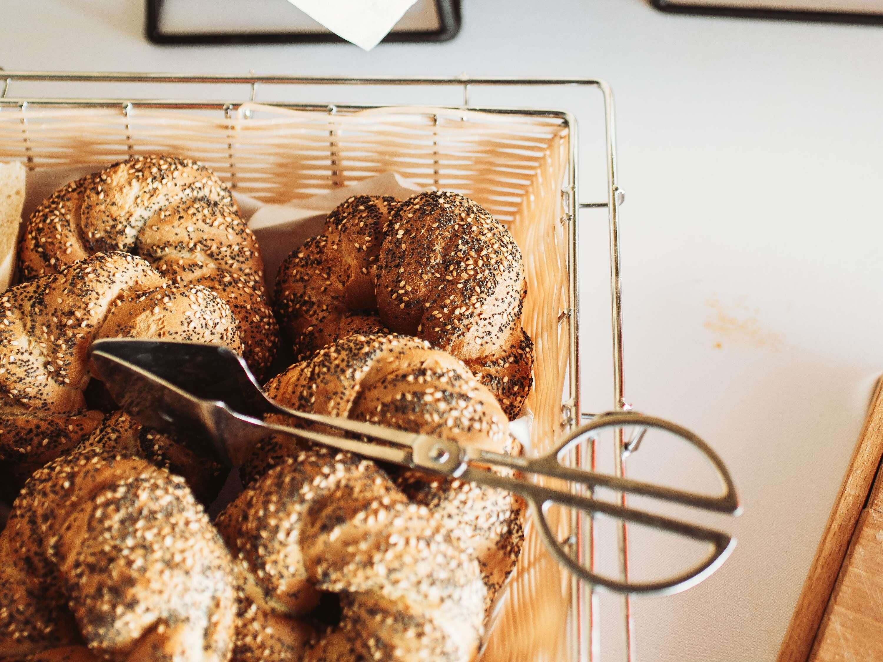 Un panier rempli de bagels fraîchement cuits, saupoudrés de graines de sésame, posé sur une grille métallique.