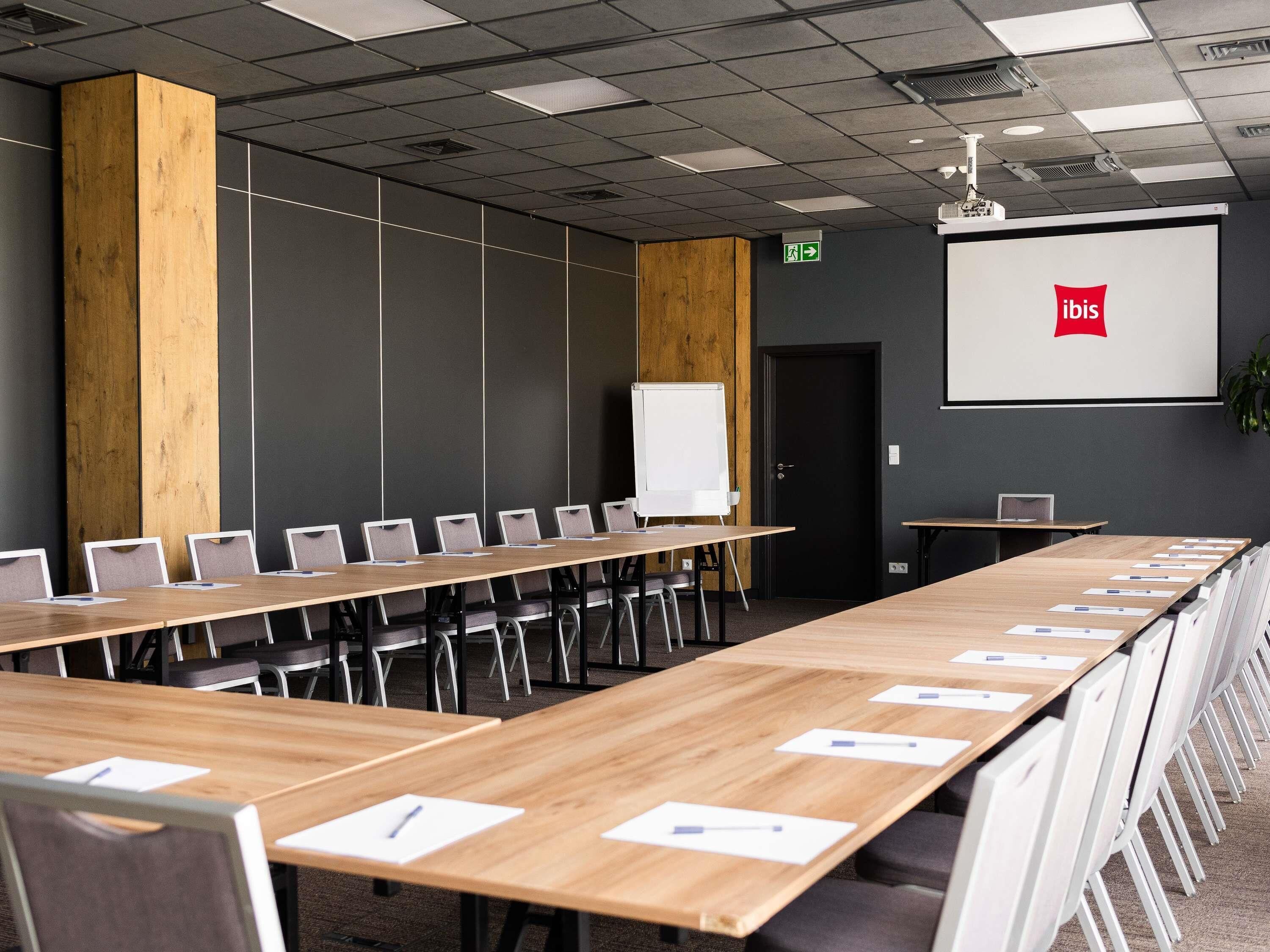 A conference room with a long table, chairs, a whiteboard, and a projector screen displaying the ibis logo.