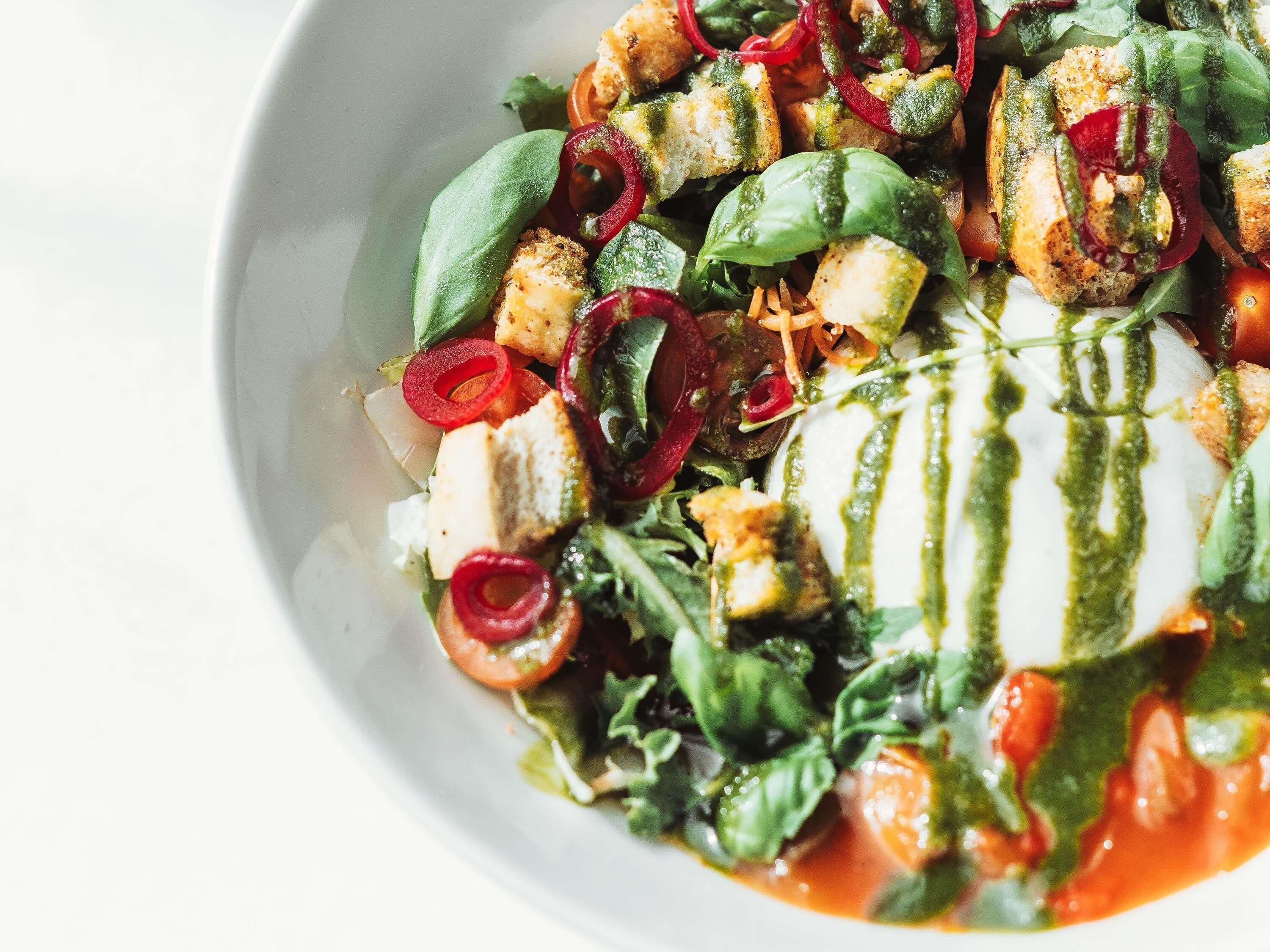 A bowl of salad with various vegetables and a drizzle of green sauce.