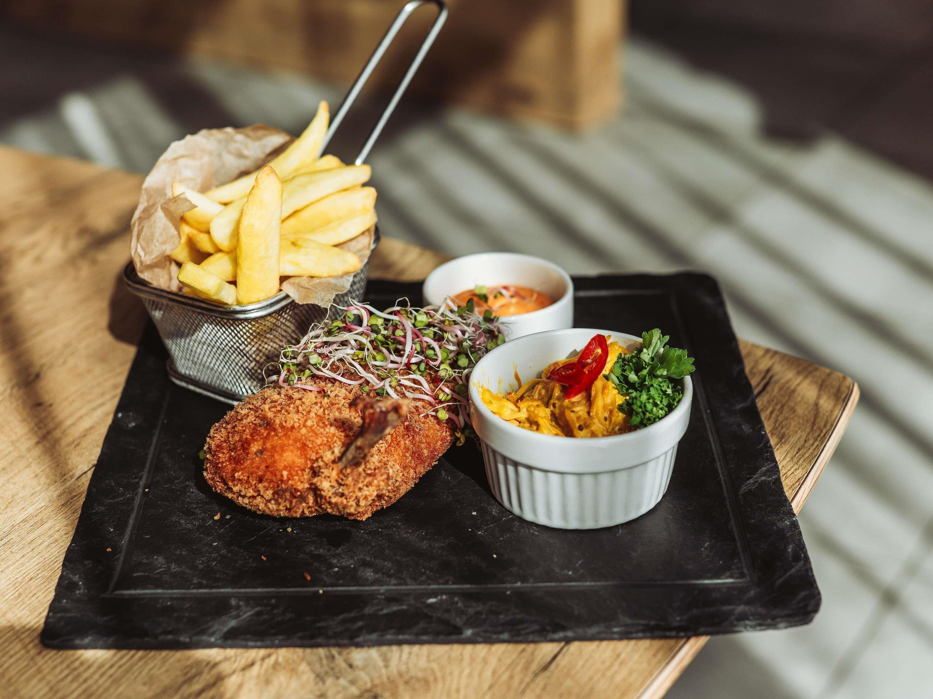 En bakke med en paneret schnitzel, pommes frites, en salatskål og to dressinger.