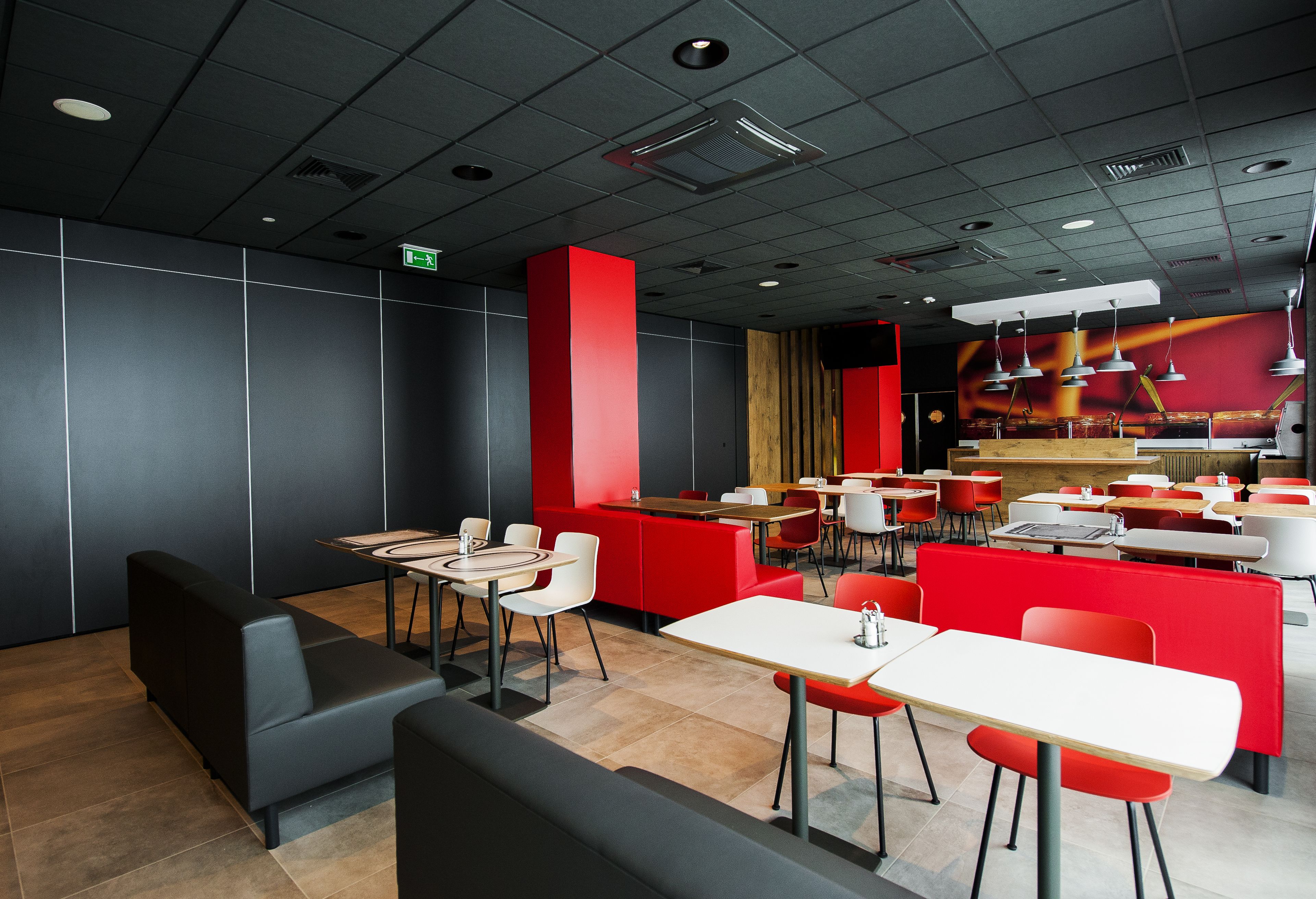 Un interior de restaurante moderno con asientos negros y rojos, mesas blancas y una pared de acento roja.