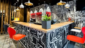 Zona de bar con mostrador, sillas rojas y lámparas colgantes.