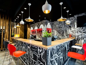 Un espace bar avec un comptoir, des chaises rouges et des lampes suspendues.
