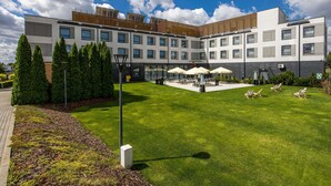 Un hotel moderno con patio, mobiliario exterior y césped bien cuidado.