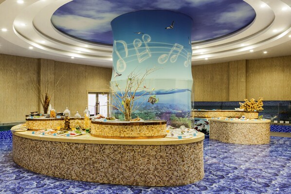 Un área de recepción con un pilar central que presenta un mural de notas musicales y gaviotas, rodeado de un piso de baldosas y un acuario grande.